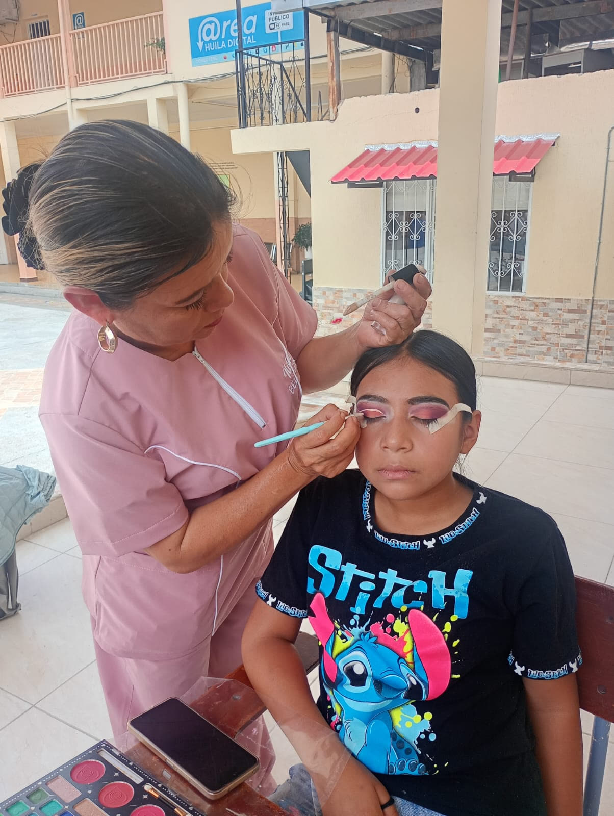 Docente aplicando maquillaje de ojos a una estudiante