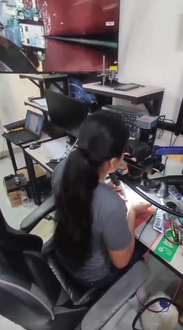 Estudiante reparando la placa de un celular con microscopio